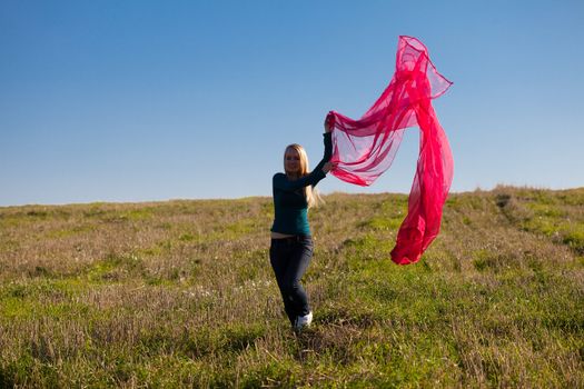 young beautiful woman jumping with tissue into the field against the sky