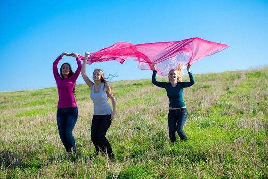 three young beautiful woman jumping with tissue into the field against the sky