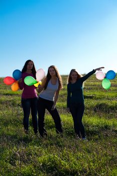 three young beautiful woman with balloons into the field against the sky