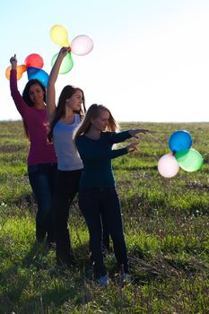 three young beautiful woman with balloons into the field against the sky