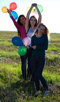 three young beautiful woman with balloons into the field against the sky