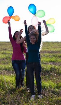 three young beautiful woman with balloons into the field against the sky