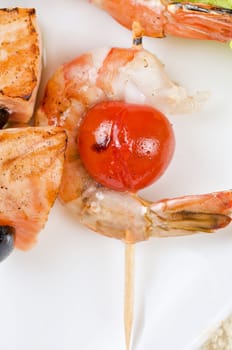 Closeup of grilled shrimps and tomatoes on bamboo sticks with salmon