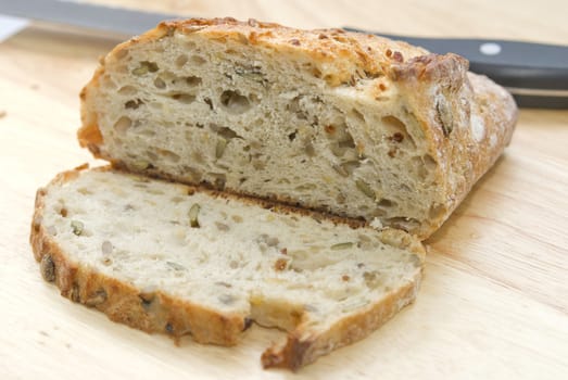 Loaf of bio bread with different seeds on the wooden table, knife in the background