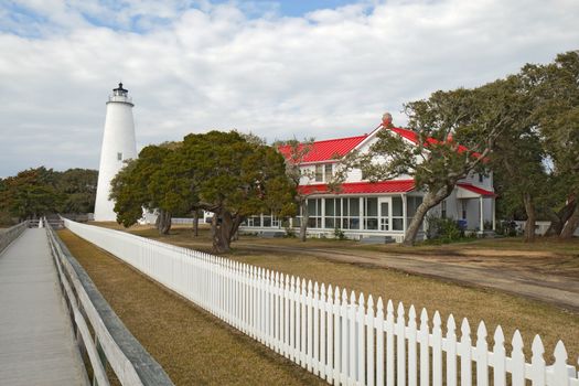 White picket fence and walkway lead past the red-roofed keepers quarters towards the tower of the Ocracoke Island lighthouse on the outer banks of North Carolina, the second-oldest operating lighthouse in the United States