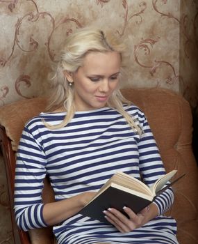 Young and beautiful girl reading a book cover in black sitting on a couch in his home