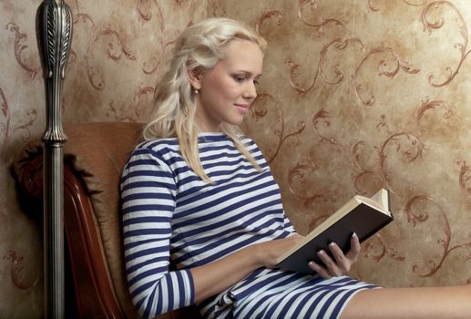 Young and beautiful girl reading a book cover in black sitting on a couch in his home