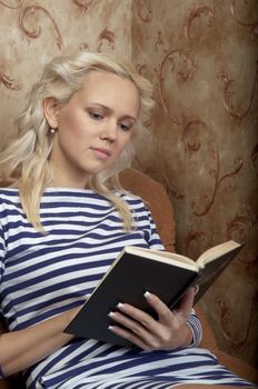 Young and beautiful girl reading a book cover in black sitting on a couch in his home