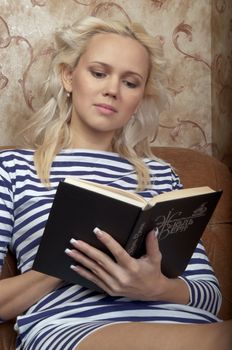 Young and beautiful girl reading a book cover in black sitting on a couch in his home