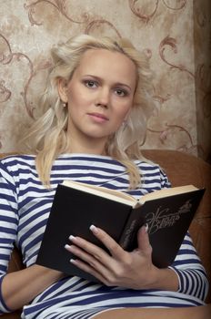 Young and beautiful girl reading a book cover in black sitting on a couch in his home