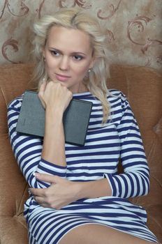 Young and beautiful girl reading a book cover in black sitting on a couch in his home