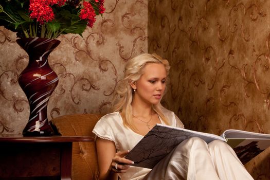 Young and beautiful girl reading a book cover in black sitting on a couch in his home