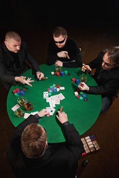 Photo of four men playing poker, smoking cigars and drinking whiskey.