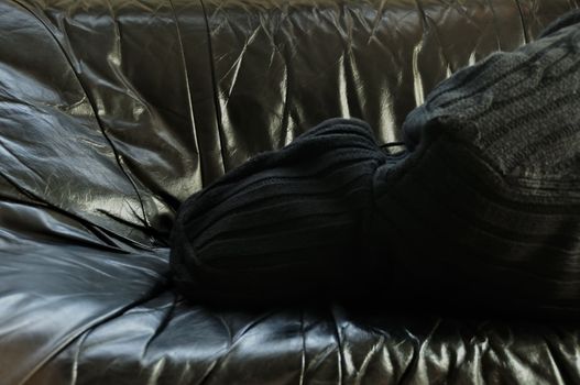 Hooded man sleeping on black couch.