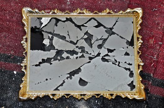 Antique golden picture frame with broken glass on dirty rag background.