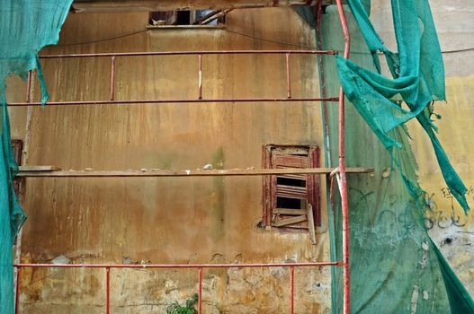 Abandoned building with torn debris netting broken window and grungy wall.