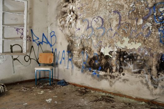 Chair in decayed room interior. Peeling moldy wall and smudged paint.