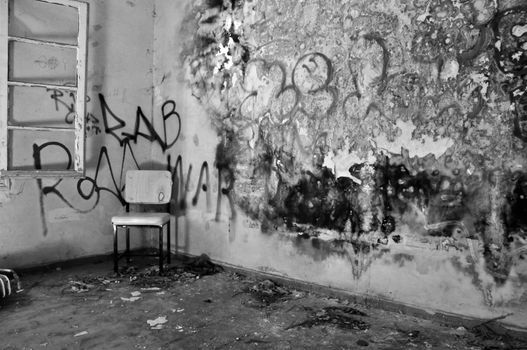 Chair in the corner of a decayed room with peeling moldy wall. Black and white.