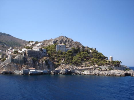 Hydra rocky beach with old buildings close to town                               
