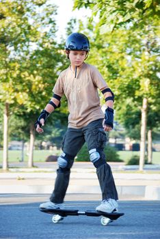 Teenage boy riding a skateboard in a parking lot with trees in the background on a sunny day.