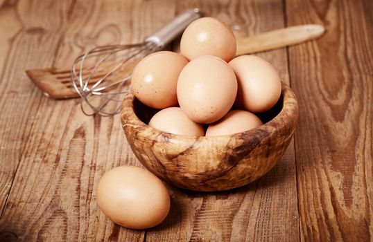 fresh brown eggs with egg whisk on wooden background