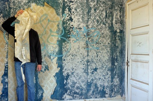 Male figure behind torn wallpaper shred in abandoned building interior.
