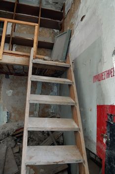 Steep wooden staircase crumbling attic and fire extinguisher sign in abandoned factory interior.