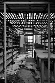 Rows of empty shelves in abandoned factory storage room. Black and white.