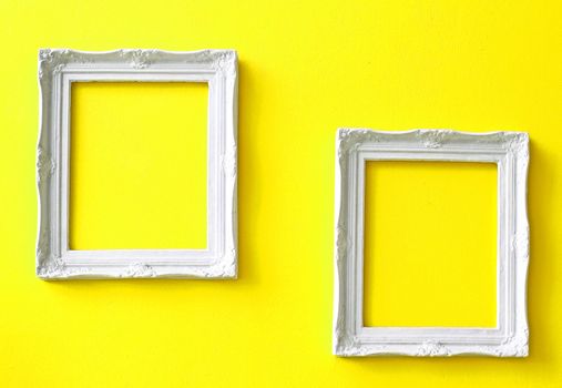 Two white vintage frames on yellow wall 