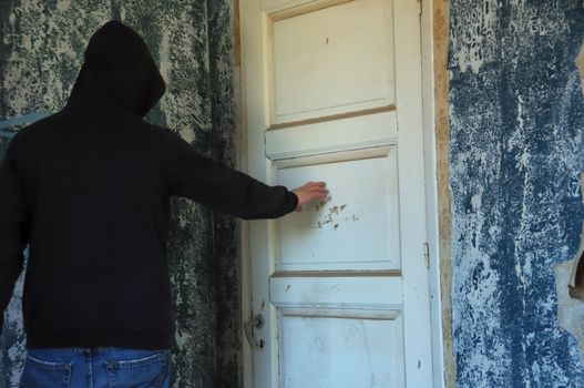 Ghostly hooded figure by the closed door of a decayed room. Abandoned house interior.