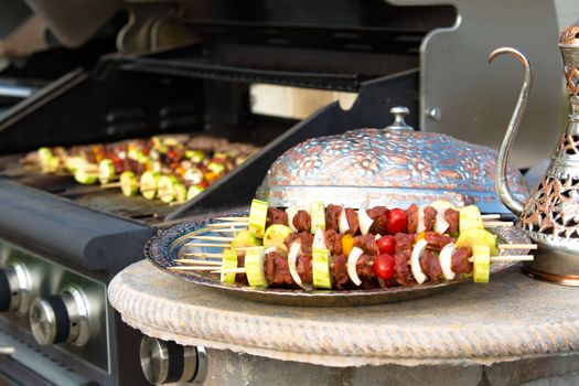 Meat skewers with vegetables waiting their turn to be grilled in traditional and authentic looking copper plate complimenting pitcher.