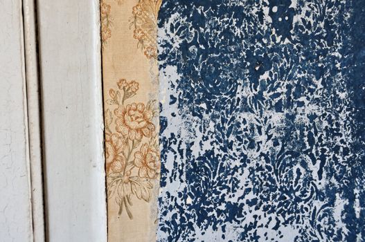 Torn vintage wallpaper and floral pattern imprinted on peeling paint wall.