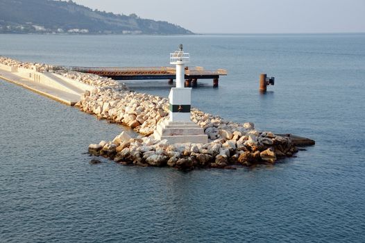�utomated lighthouse by the sea and rock jetty breakwater at port entrance.