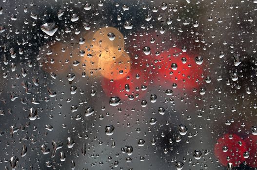 Raindrops on glass surface and blurry abstract city lights. Background texture.