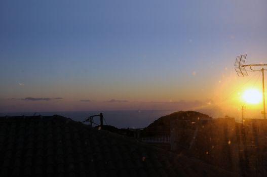 Sunset light reflected through stained window glass and over village rooftops.