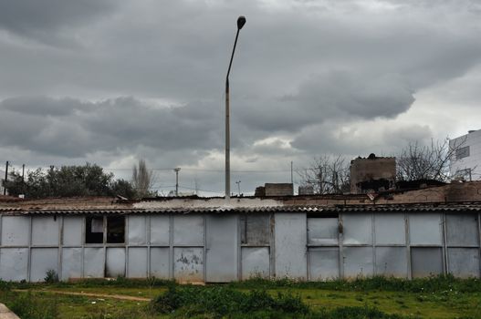 Rusty warehouse shack under moody sky. Street light emerging through the roof drying laundry by the window.