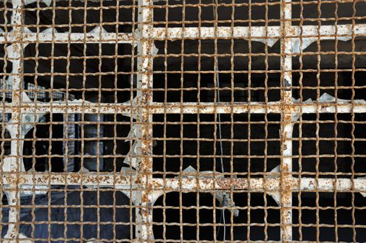 Broken industrial window wire mesh in abandoned warehouse. Rusty metal texture.