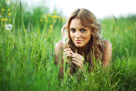 girl blow on dandelion on green field