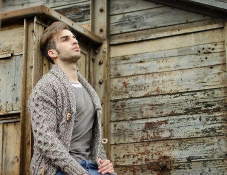 Good looking guy leaning against rusty metal and wooden walls