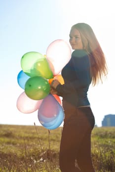 young beautiful woman with balloons into the field against the sky
