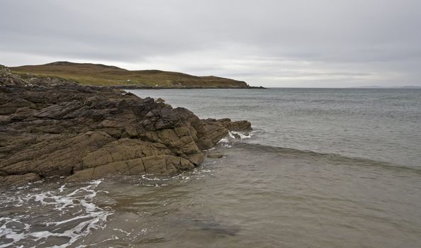 stoney coastline in scotland with small hill in background