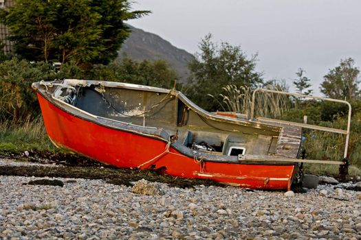 read boat at coast in scotland with trees in background