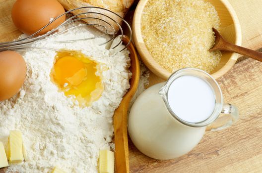 Preparing Dough. Ingredients with Jar of Milk, Flour, Butter, Eggs, Sugar and Wooden Spoon with Egg Whisk closeup on Wooden background. Top View