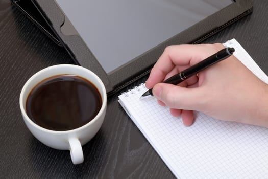 Closeup of a male hand writing notes on notepad at desk