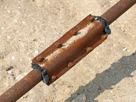 Damaged rusty water pipe on a sand background.