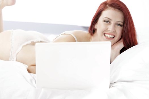 Attractive young woman working on her laptop in white underwear on her bed at home