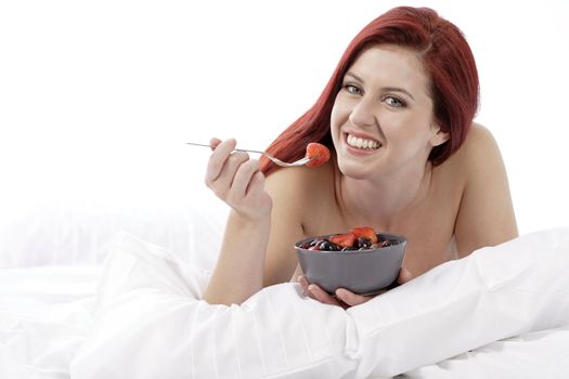 Attractive young woman on her bed at home eating fresh fruit for breakfast