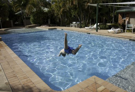 teenage boy jumping into a swimming pool in summer