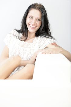 Attractive young woman sitting on a white sofa in casual clothes smiling