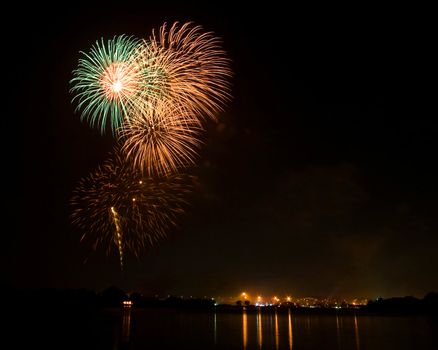 Green and Orange Fireworks at lake on King Birthday Festival and Holiday in Thailand.